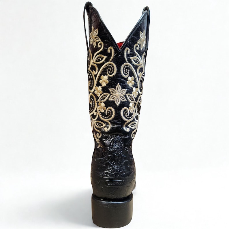 May include: Black leather cowboy boot with gold floral embroidery. The boot has a pointed top and a block heel. The interior is lined with red fabric. A classic Western-style boot.