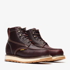 May include: A pair of dark brown leather work boots with white stitching and a tan sole. The boots have a lace-up design with metal eyelets and a yellow tag on the side. The boots are designed for work and have a sturdy construction.