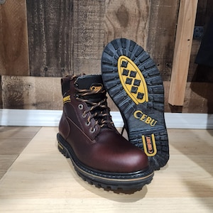 May include: A pair of brown leather work boots with black soles and orange laces. The boots have the brand name "CEBU" on the side and sole. The soles are designed for comfort and traction.