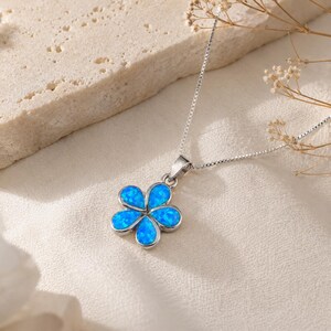 May include: A silver-toned necklace featuring a flower-shaped pendant with five teardrop-shaped petals inlaid with iridescent blue opal-like material. The pendant is attached to a delicate silver-toned box chain that extends upward.