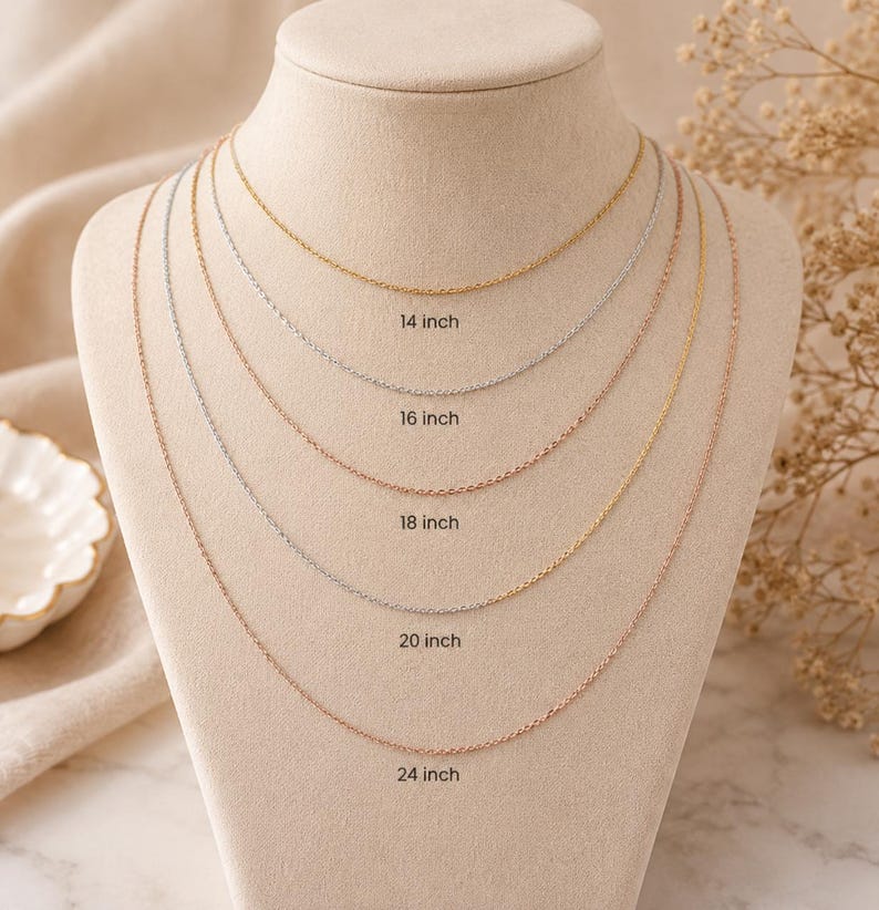 May include: A display of delicate chain necklaces in gold, silver, and rose gold, each with a different length. The lengths are labeled as 14 inch, 16 inch, 18 inch, 20 inch, and 24 inch. The necklaces are draped on a mannequin.