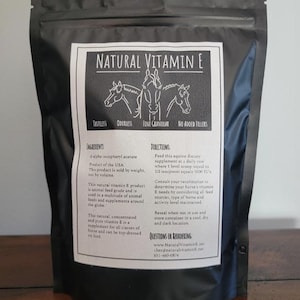 Może przedstawiać: Biały worek z czarnym zamkiem błyskawicznym. Worek zawiera naturalny suplement witaminy E dla koni. Worek ma etykietę z napisem "Natural Vitamin E" i obrazkiem trzech koni. Etykieta zawiera również napisy "Bez smaku", "Bez zapachu", "Drobnoziarnisty" i "Bez dodatków".