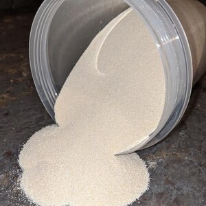 May include: A clear plastic container with a white powder spilling out onto a gray surface.