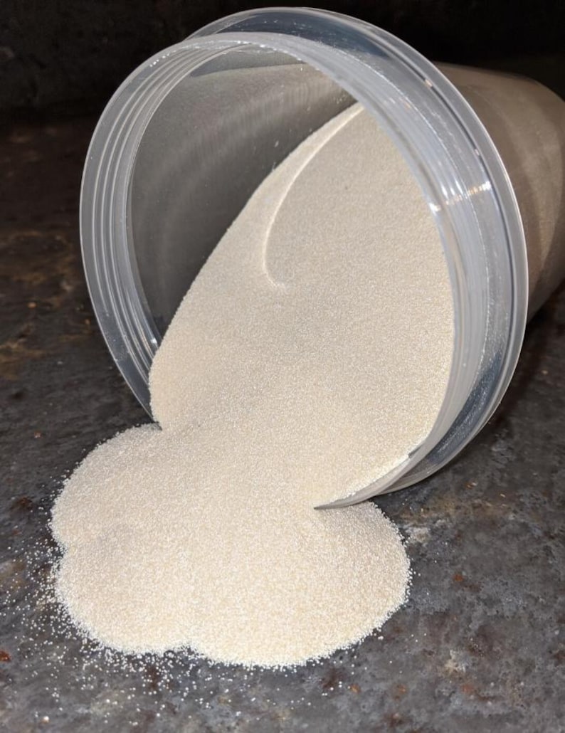 May include: A clear plastic container with a white powder spilling out onto a gray surface.