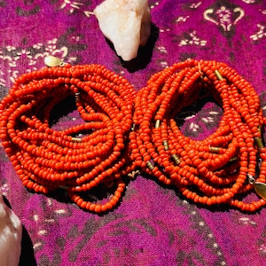 May include: Two sets of orange beaded jewelry with gold accents. The beads are small and round, and the jewelry is arranged in a circular shape.