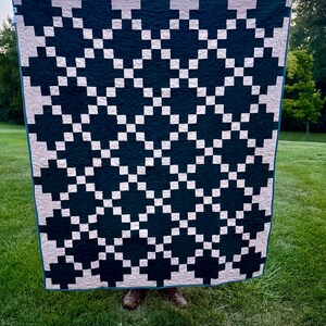 May include: A handmade quilt with a geometric pattern of dark teal and white squares. The quilt is displayed outdoors on a sunny day, showcasing its intricate design and craftsmanship. The quilt's edges are finished with a teal border.