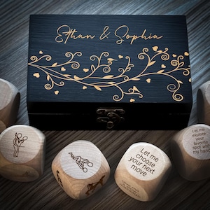 May include: A wooden box with a black lid and gold floral design. The lid is engraved with the names "Ethan & Sophia". The box contains six wooden dice with various suggestive phrases and illustrations.