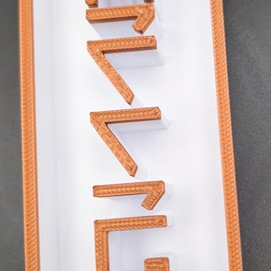 May include: A white plaque with an orange border and the word "GENUINE" written in orange raised letters.