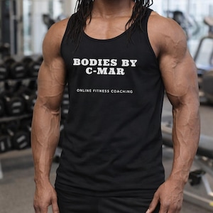 May include: Black tank top with the text "BODIES BY C-MAR" and "ONLINE FITNESS COACHING" in white. The tank top is sleeveless and worn in a gym setting.
