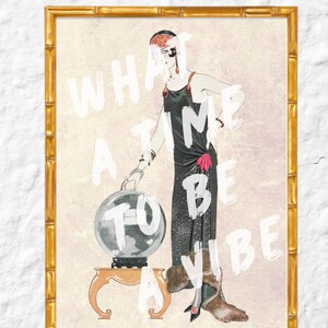 Puede incluir: Ilustración vintage enmarcada de una mujer con un vestido negro con una bola de cristal sobre una pequeña mesa. El texto "WHAT A TIME TO BE A VIBE" está superpuesto en blanco. El marco es dorado.