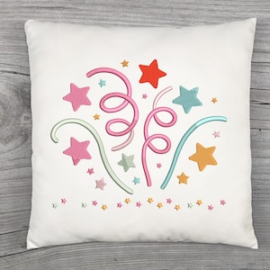 Puede incluir: Cojín cuadrado blanco con un diseño bordado de estrellas y serpentinas de colores. El diseño incluye estrellas rosas, naranjas, azules y verdes, junto con serpentinas rosas y verdes, creando un tema festivo.