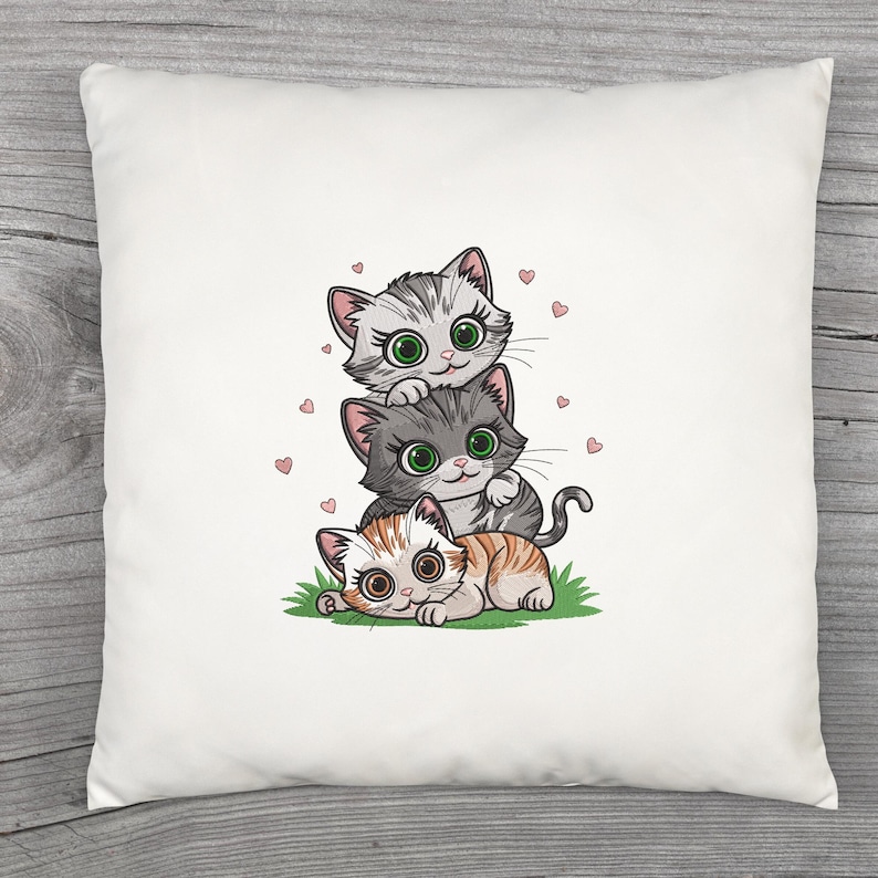 May include: White square pillow featuring a stack of three cartoon cats. The top cat is gray and white, the middle cat is gray, and the bottom cat is orange and white. Pink hearts are scattered around the cats.