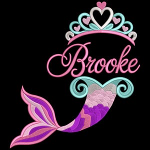May include: A mermaid design with the name "Brooke" embroidered in pink script. The design features a pink, blue, and white crown with heart accents above the name. The mermaid tail is a mix of pink, purple, and white.