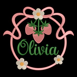May include: Pink embroidered design featuring the name "Olivia" in green script, surrounded by a pink ribbon and three pink strawberries with green leaves. White flowers with yellow centers are placed around the design on a black background.