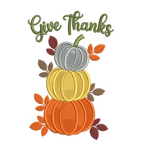 May include: An embroidered design featuring three stacked pumpkins in orange, yellow, and silver, with green stems and fall leaves. The words "Give Thanks" are written in green script above the pumpkins, perfect for fall decor.