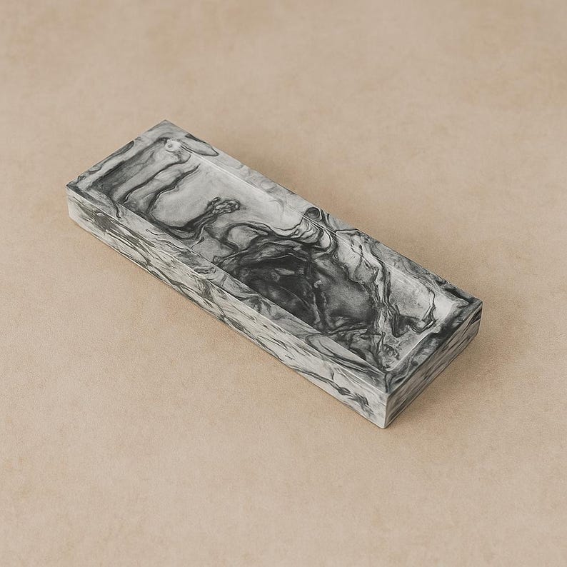 May include: A rectangular tray with a marbled gray and white pattern. The tray has a shallow, open design and is made of a solid material. The surface has a swirling, organic design. The tray is suitable for holding small items.