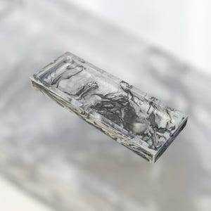 May include: A rectangular tray with a marbled pattern in shades of gray and white. The tray has a raised edge and a smooth, glossy finish. The design resembles natural stone, adding a touch of elegance.