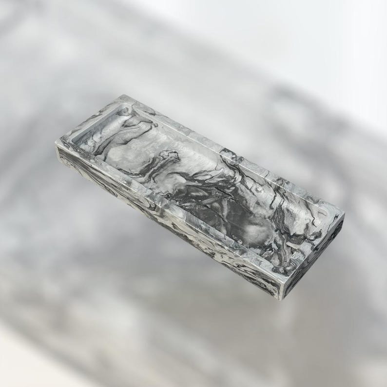 May include: A rectangular tray with a marbled pattern in shades of gray and white. The tray has a raised edge and a smooth, glossy finish. The design resembles natural stone, adding a touch of elegance.