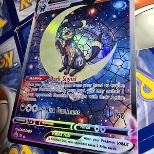 May include: Umbreon VMAX Pokémon card featuring a black and blue creature on a crescent moon with a stained-glass background. The card has the text "Dark Signal" and "Max Darkness" with a 160 attack. The card is a Single Strike card.