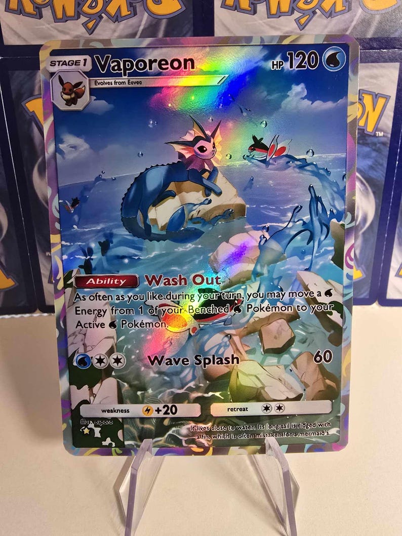 May include: A holographic Vaporeon Pok&eacute;mon trading card. The card features a blue and pink Vaporeon character in a water-themed scene. The card has text that reads "Vaporeon", "Wash Out", and "Wave Splash".