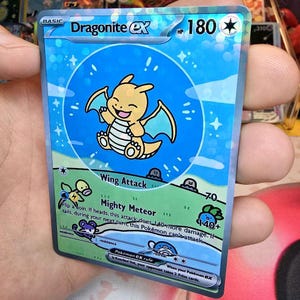 Puede incluir: Carta coleccionable Pokémon Dragonite EX holográfica. La carta presenta un personaje de dibujos animados Dragonite en un círculo azul con un fondo azul claro. El texto "Dragonite EX" y "180 HP" es visible.