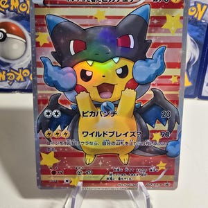Puede incluir: Una carta de comercio de Pokemon con Pikachu usando una capa azul y negra con detalles rojos. La carta se titula "Pikachu con una capa" y tiene 70 PS. La carta tiene dos ataques: "Pika Punch" por 20 de daño y "Wild Blaze?" por 90 de daño. La carta es de la serie XY.