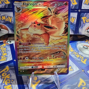 May include: A holographic Flareon EX Pok&eacute;mon trading card. The card features a fiery orange and yellow illustration of Flareon, with the text "Flareon EX" and "HP 150". The card is displayed in a clear plastic holder.