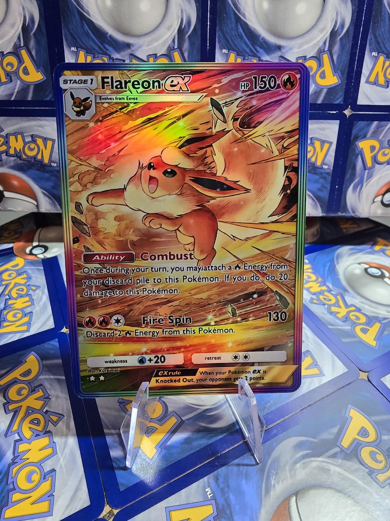 May include: A holographic Flareon EX Pok&eacute;mon trading card. The card features a fiery orange and yellow illustration of Flareon, with the text "Flareon EX" and "HP 150". The card is displayed in a clear plastic holder.