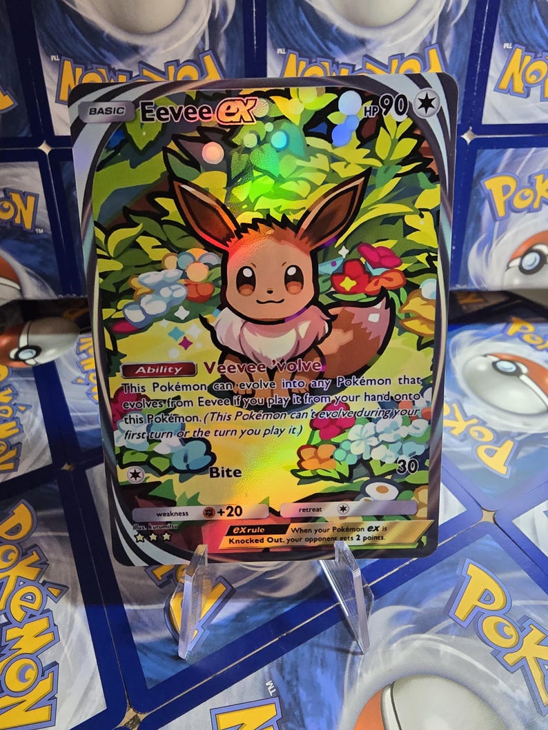 May include: A holographic Eevee EX Pok&eacute;mon trading card. The card features a colorful illustration of Eevee surrounded by flowers and foliage. The card has text that includes "Basic", "HP 90", "Veevee Volve", and "Bite".