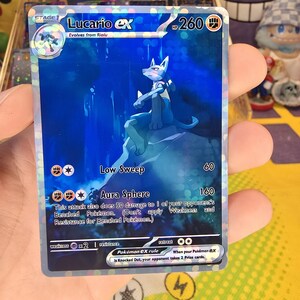 K&ouml;nnte beinhalten: Eine holografische Lucario EX Pok&eacute;mon-Sammelkarte. Die Karte zeigt einen blauen Lucario-Charakter mit dem Text "Lucario EX" und "Aura Sphere". Die Karte hat 260 HP und den Text "Evolves from Riolu".