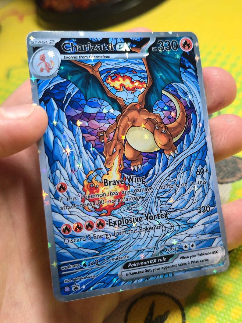 K&ouml;nnte beinhalten: Eine Charizard EX Pok&eacute;mon-Sammelkarte. Die Karte zeigt eine lebendige Illustration von Charizard mit blauen Fl&uuml;geln und einem feurigen Schwanz, vor einem Hintergrund im Buntglasstil. Die Karte hat den Text "Brave Wing" und "Explosive Vortex".