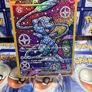 Może przedstawiać: Holograficzna karta kolekcjonerska Pokémon Mew ex. Karta przedstawia witrażową ilustrację Mew w odcieniach niebieskiego, fioletowego i zielonego. Karta ma złote obramowanie i zawiera tekst, taki jak "Genome Hacking" i "Restart".
