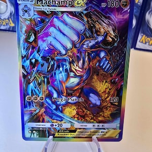 May include: A holographic Machamp EX Pok&eacute;mon trading card. The card features a dynamic illustration of Machamp in action, with a blue and orange color scheme. The card has the text "Mega Punch" and "HP 180".