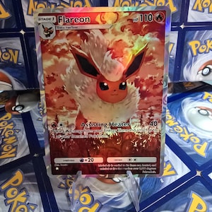 May include: A holographic Flareon Pok&eacute;mon card. The card features a fiery orange and white creature with black ears and a smiling face. The card has text including "Flareon", "HP 110", and "Assisting Heater".