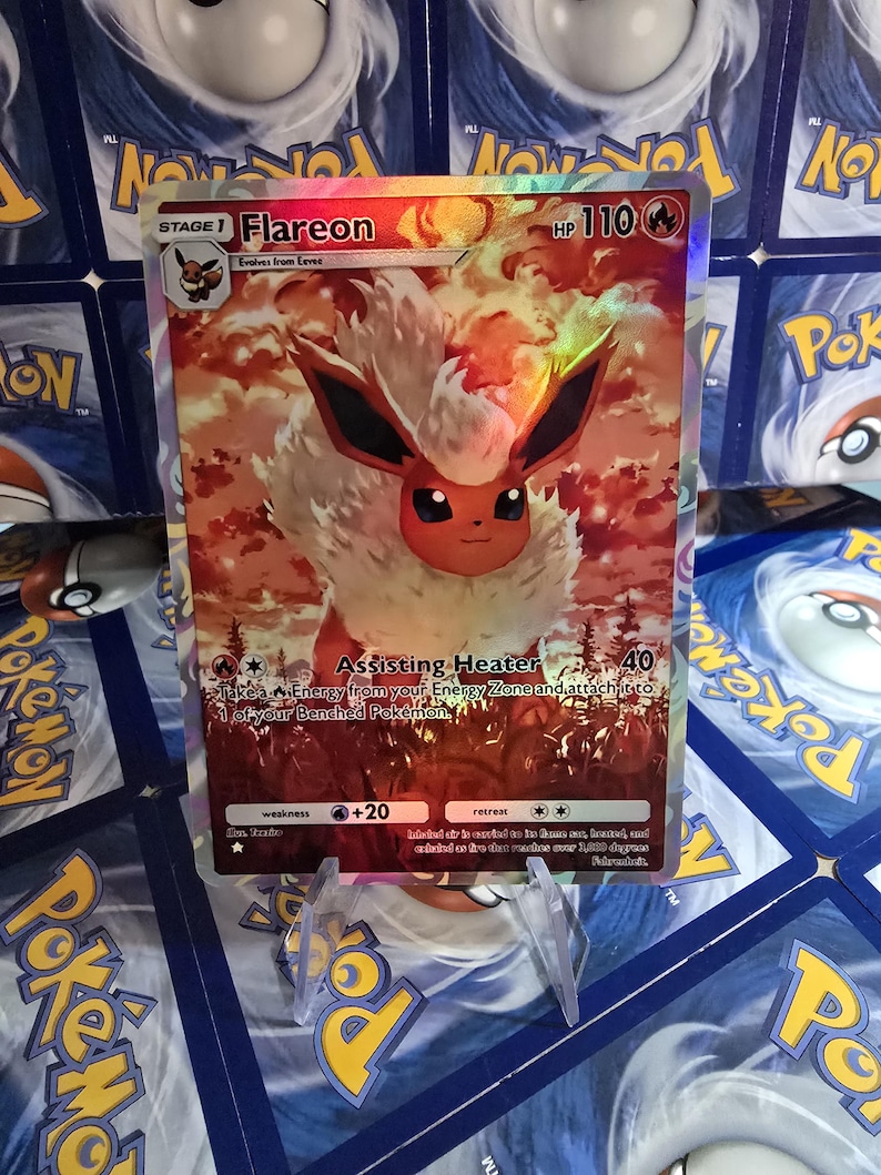 May include: A holographic Flareon Pok&eacute;mon card. The card features a fiery orange and white creature with black ears and a smiling face. The card has text including "Flareon", "HP 110", and "Assisting Heater".