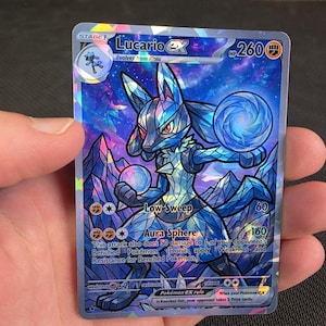 May include: A Lucario ex trading card with a holographic stained-glass art style. The card features the character Lucario in blue and purple tones, holding glowing spheres. Text includes Lucario ex, 260 HP, Low Sweep, and Aura Sphere.