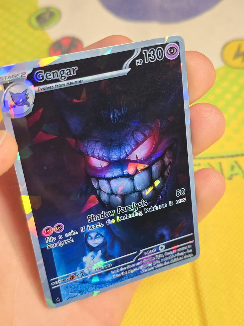 K&ouml;nnte beinhalten: Holografische Gengar Pok&eacute;mon-Karte. Die Karte zeigt ein dunkelviolettes Gengar mit roten Augen und einem breiten Grinsen. Der Text "Gengar" und "Shadow Paralysis" sind vorhanden.