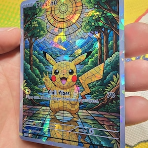Puede incluir: Carta coleccionable holográfica de Pikachu con una ilustración estilo vidriera. La carta presenta un personaje Pikachu amarillo con el texto "Chill Vibes". La carta tiene 120 HP y un coste de retirada de una estrella.