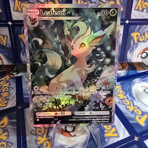 May include: A holographic Leafeon Pok&eacute;mon card. The card features a light green and cream-colored Leafeon character with a forest background. The card has the text "Leafeon" and "Leaf Blast".