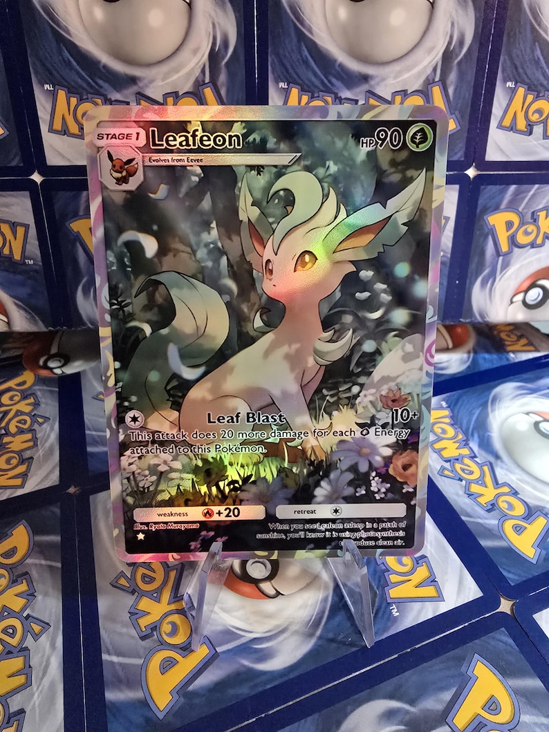 May include: A holographic Leafeon Pok&eacute;mon card. The card features a light green and cream-colored Leafeon character with a forest background. The card has the text "Leafeon" and "Leaf Blast".
