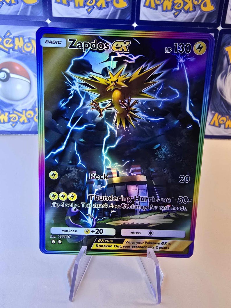 May include: A holographic Zapdos EX Pok&eacute;mon trading card. The card features a yellow bird-like creature with lightning effects. Text includes "Zapdos EX", "HP 130", and attack descriptions. The card is displayed in a clear plastic holder.