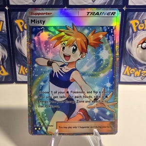 May include: A holographic Misty Trainer card from the Pok&eacute;mon Trading Card Game. The card features a colorful illustration of Misty, with text that reads "Choose 1 of your Pok&eacute;mon, and flip a coin."