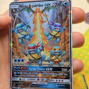 K&ouml;nnte beinhalten: Eine holografische Pok&eacute;mon-Sammelkarte mit vier Schiggy-Figuren als Ninjas, mit einem Glurak im Hintergrund. Die Karte tr&auml;gt den Text "Ninja Squirtles GX" und "Spinning Attack".
