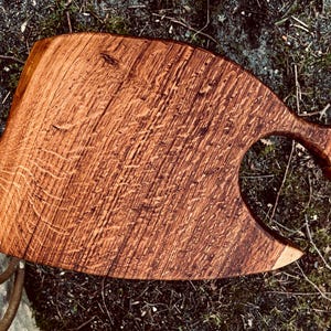 May include: A large, rustic wooden serving board shaped like a fish with a cutout for holding a bottle. The board is made of dark brown wood with a natural grain pattern.