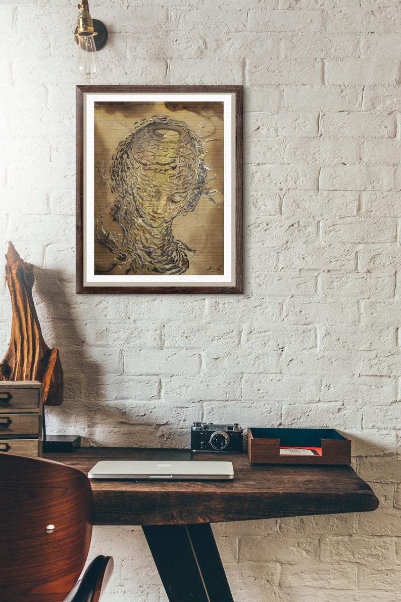 K&ouml;nnte beinhalten: Ein gerahmtes Kunstwerk, das ein stilisiertes Gesicht mit komplizierten, geschichteten Details in Gold- und Braunt&ouml;nen zeigt. Das Kunstwerk wird an einer wei&szlig;en Backsteinmauer &uuml;ber einem Holzschreibtisch mit Laptop, Kamera und Holzaccessoires ausgestellt.