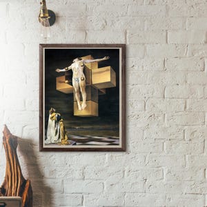 Op de afbeelding: Een ingelijste prent van een surrealistisch schilderij met een figuur op een kruis van gouden kubussen. Een persoon in een gewaad knielt eronder. De achtergrond is donker met een dambordvloer.