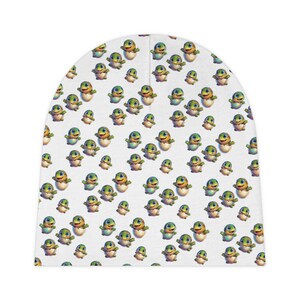 Könnte beinhalten: Weißer Beanie-Hut mit einem sich wiederholenden Muster von Cartoon-Babyschildkröten, die aus Eiern schlüpfen. Die Schildkröten sind grün, gelb und blau. Der Hut ist aus einem weichen, dehnbaren Material gefertigt.