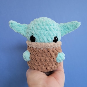 May include: A handmade plush doll in the likeness of a character from a popular science fiction series. The doll features a light blue head and ears, black eyes, and a brown and tan body. The doll is made of a soft, textured material.