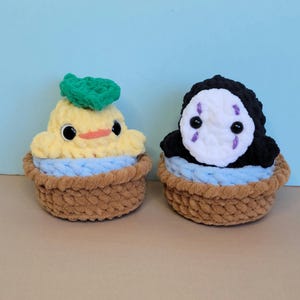 May include: Two handmade crochet plush toys. One is yellow with a green leaf, the other is black and white with purple accents. Both are in brown baskets with blue accents. The toys have black button eyes.