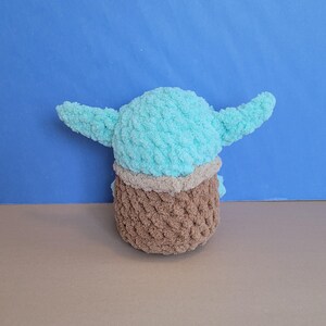 May include: A handmade plush toy in the likeness of a character with large ears. The toy features a light blue head and ears, a tan neck, and a brown body. The plush is made of a soft, textured yarn.